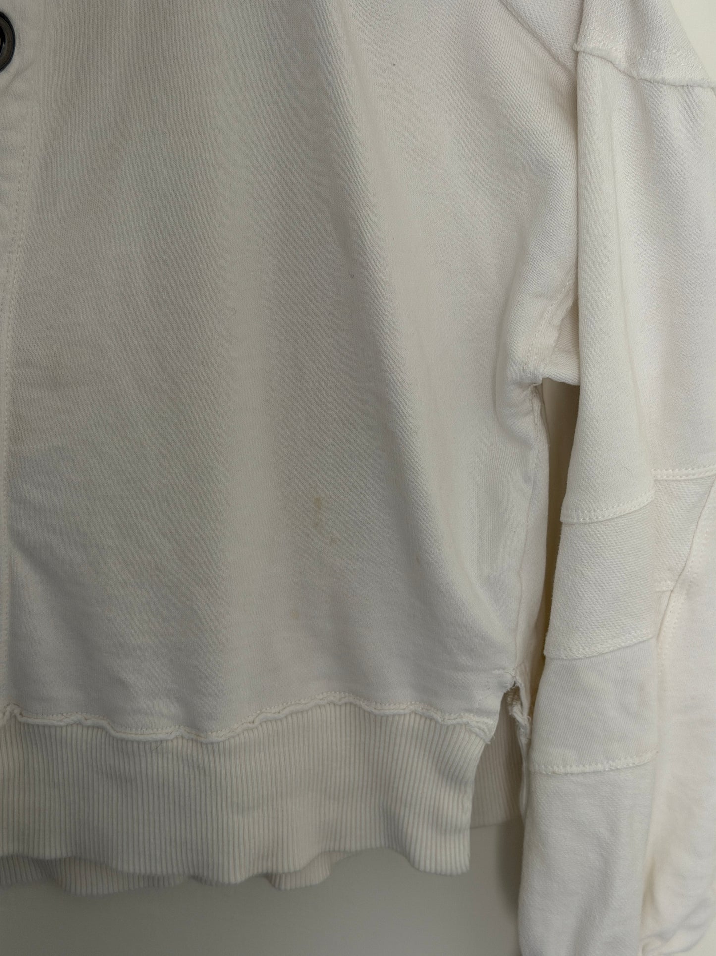 A close-up of a white fabric garment, showing the texture of the material and a ribbed cuff.