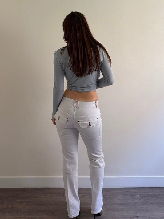 Person wearing a gray long-sleeve top and white pants standing against a plain wall.