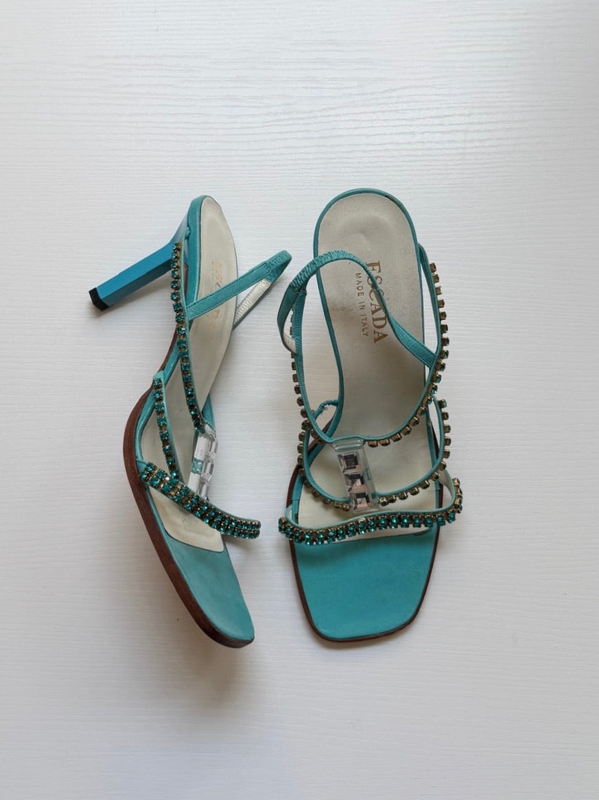 Pair of turquoise high-heeled sandals with rhinestone details on a white background