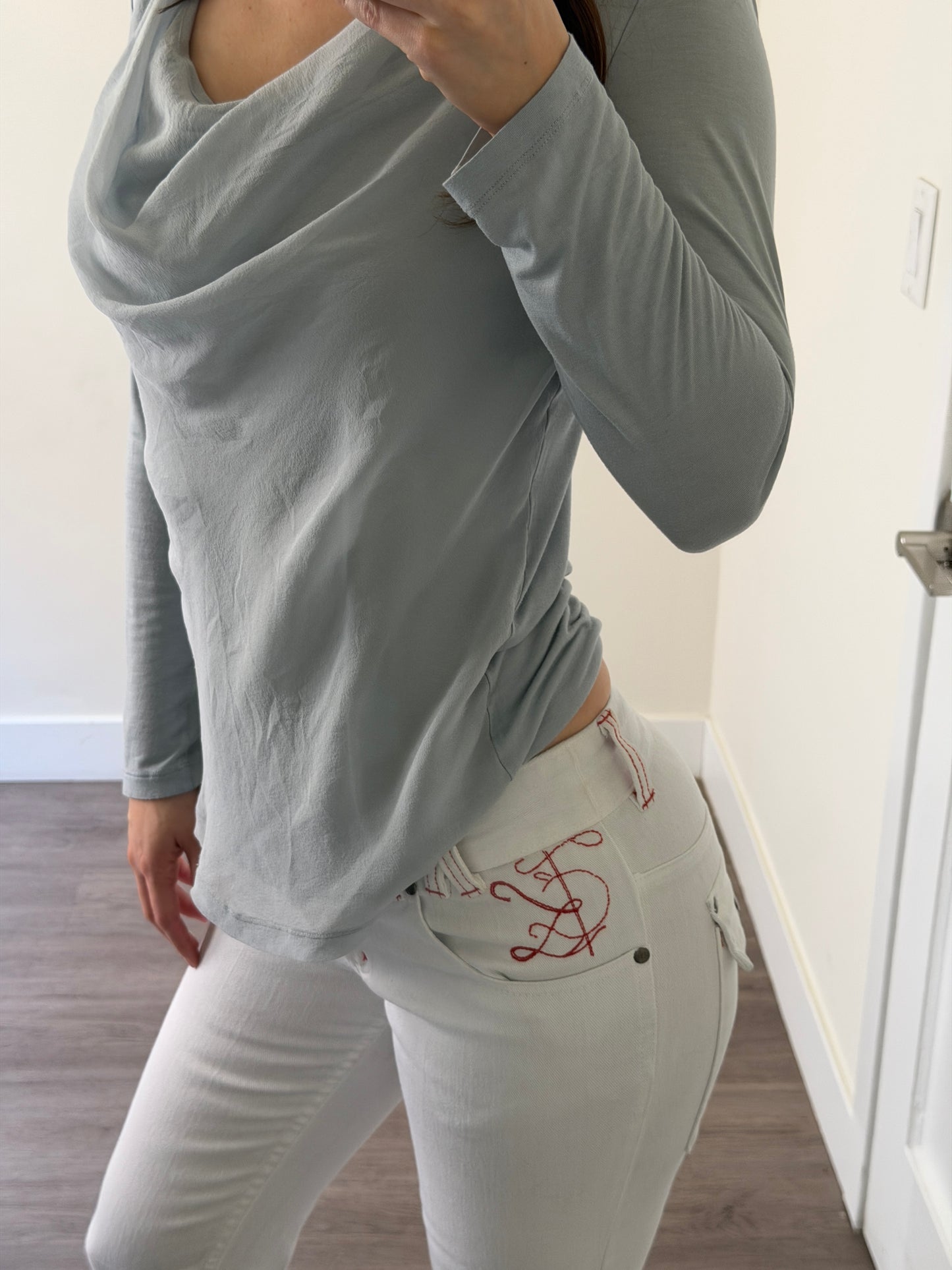 Person wearing a white shirt with a red design and gray pants in a room.