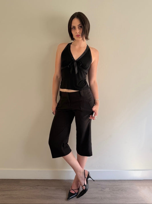 Woman wearing a black sleeveless top and black pants against a beige wall.