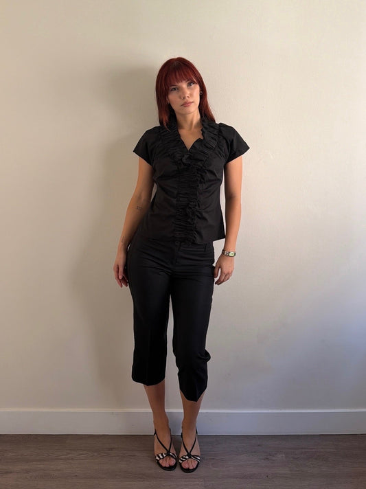 Woman wearing a black outfit standing against a plain wall.