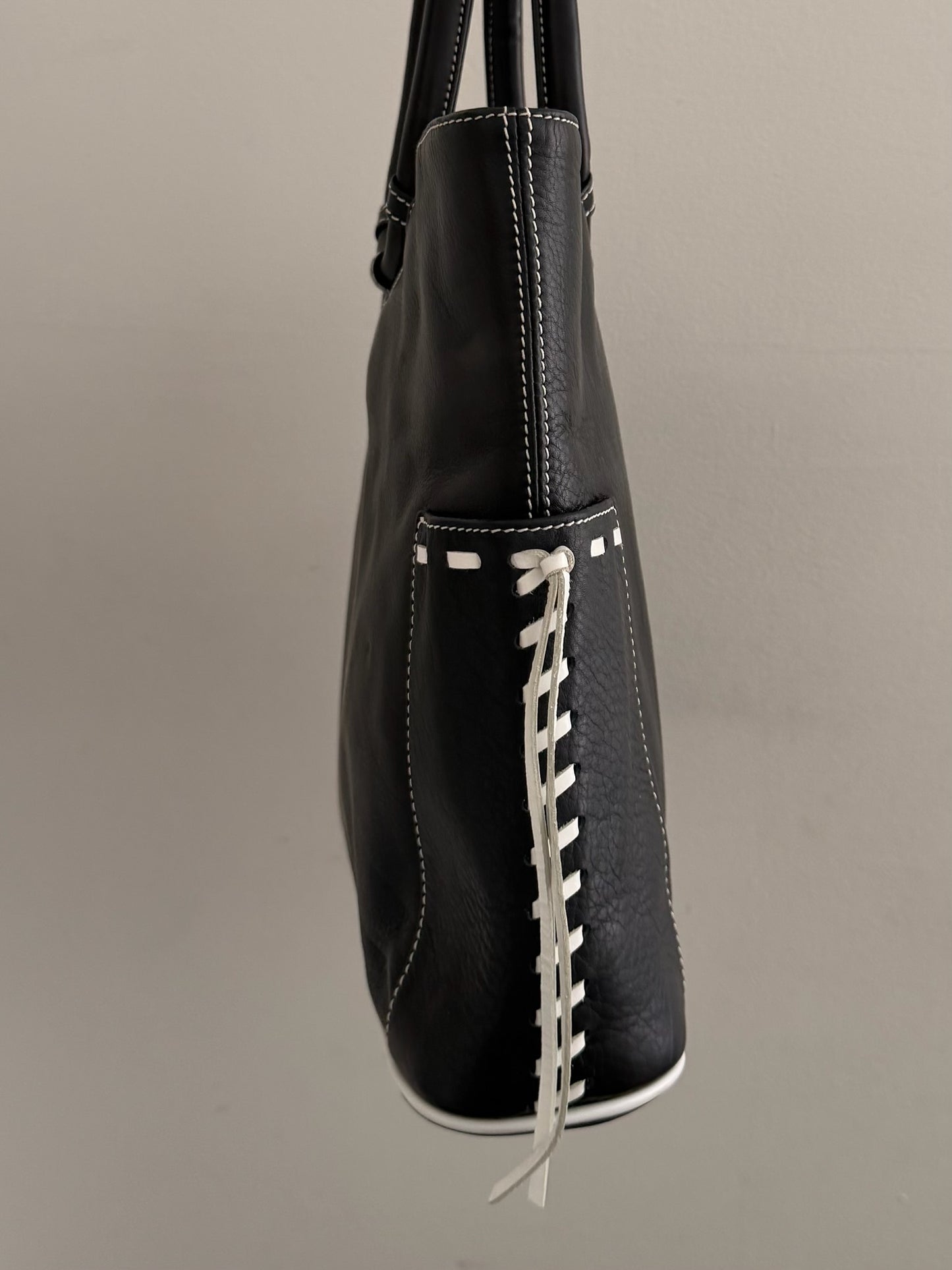 Black leather handbag with white lacing on a gray background