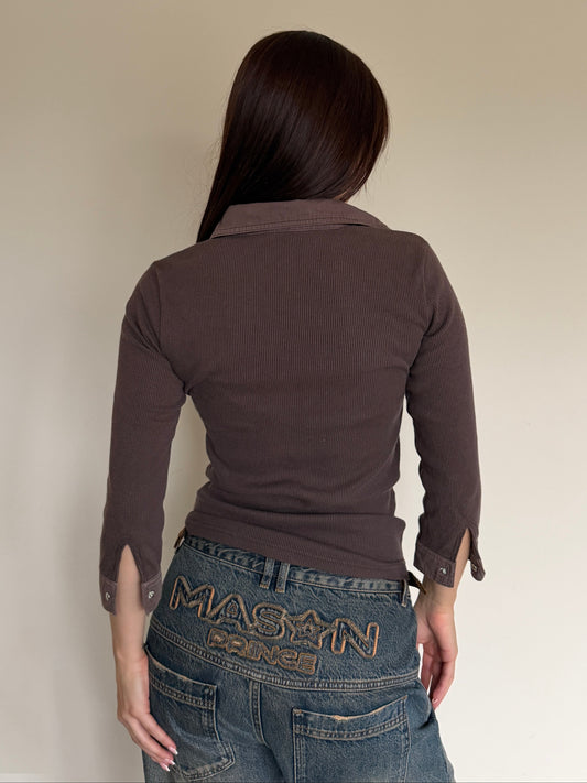 Person wearing a brown long-sleeve shirt and blue jeans with 'Maison' branding.