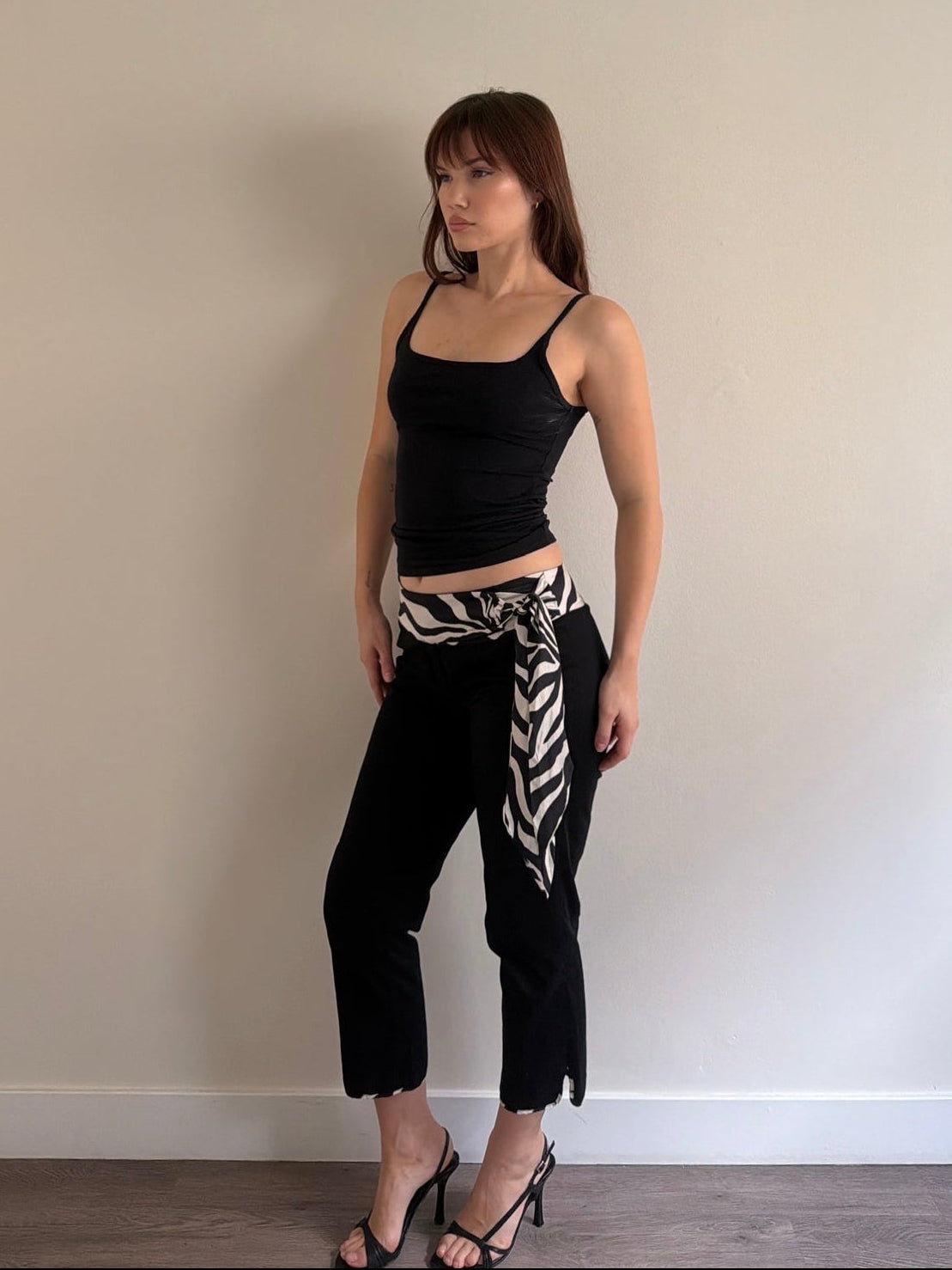 Woman wearing a black top and zebra print belt against a plain wall.
