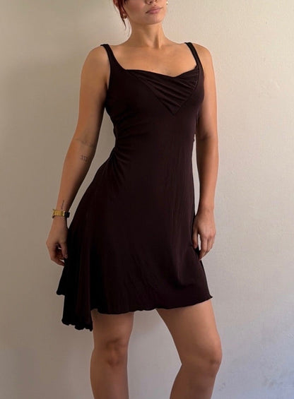 Woman wearing a black dress standing against a plain wall.