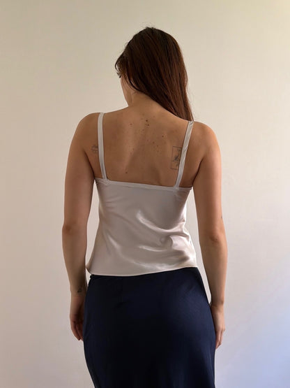 Woman wearing a white tank top and dark pants against a plain background