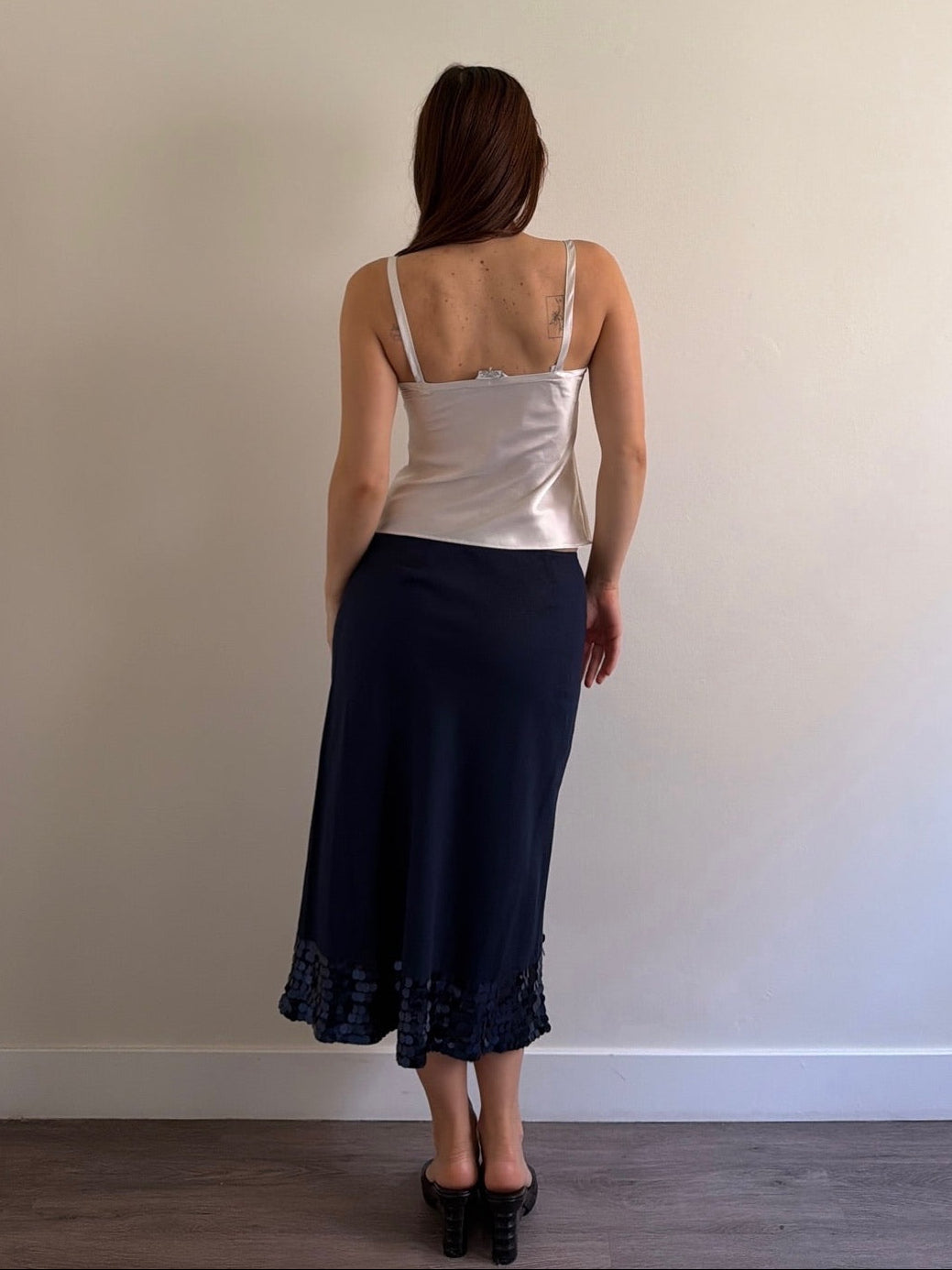 Woman wearing a white top and navy skirt against a plain wall.