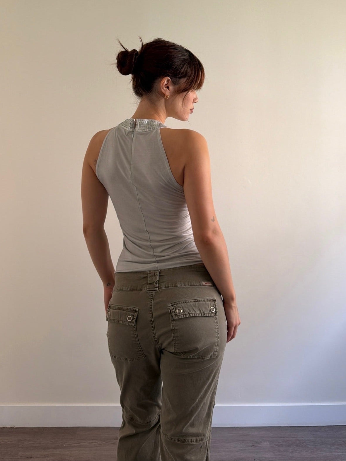 Woman wearing a gray tank top and green pants against a plain wall.