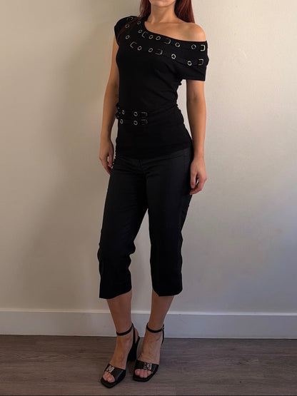 Woman wearing a black outfit with unique design elements against a plain wall.