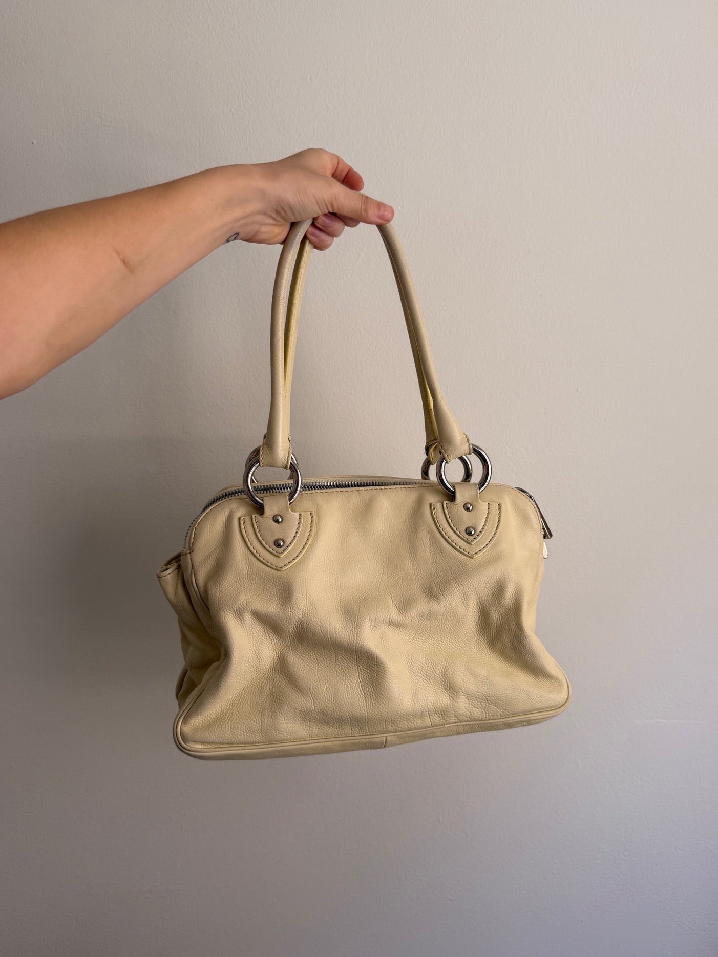 Beige handbag held by a hand against a plain background