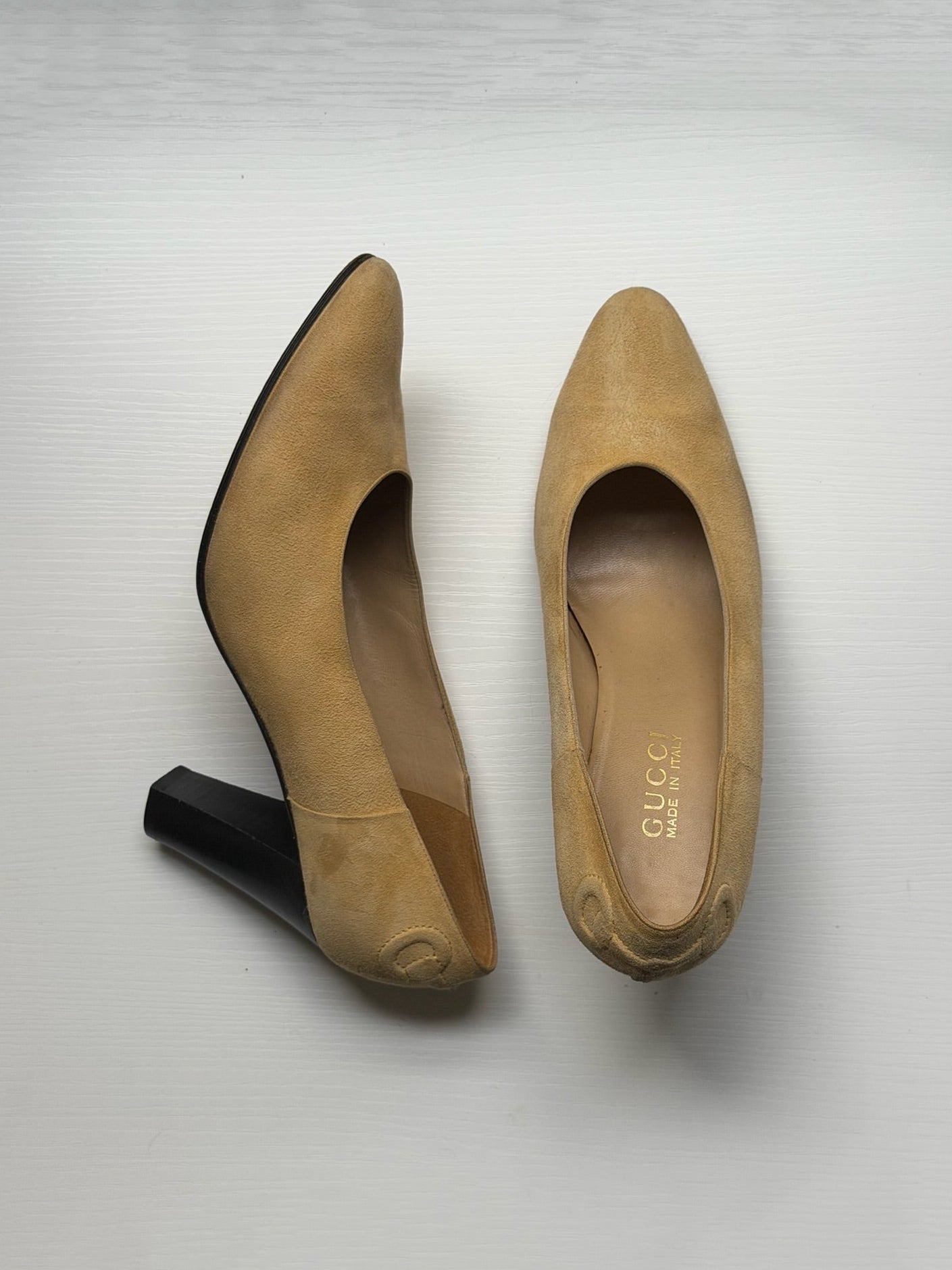 A pair of beige suede pointed-toe pumps with block heels, shown from both the side and top views on a light gray background. The brand name 'GUCCI' is visible on the insole.