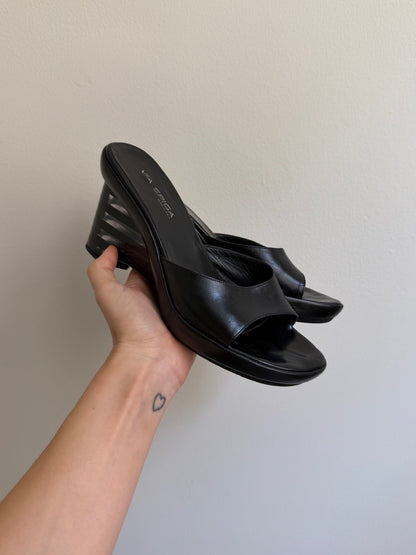 Black sandal held by a hand against a plain background