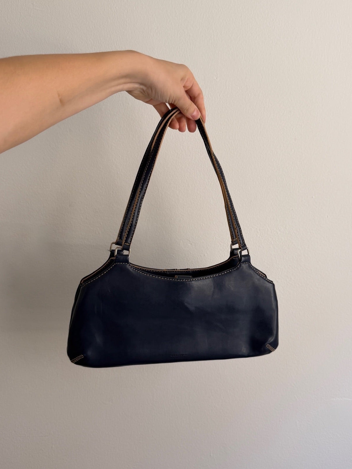 Hand holding a black handbag against a plain background