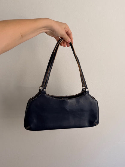 Hand holding a black handbag against a plain background