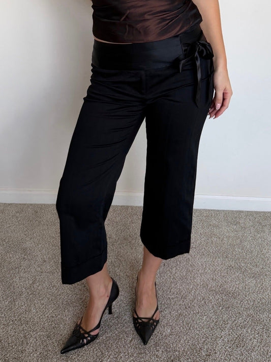 Person wearing a black strapless top and black pants against a plain background