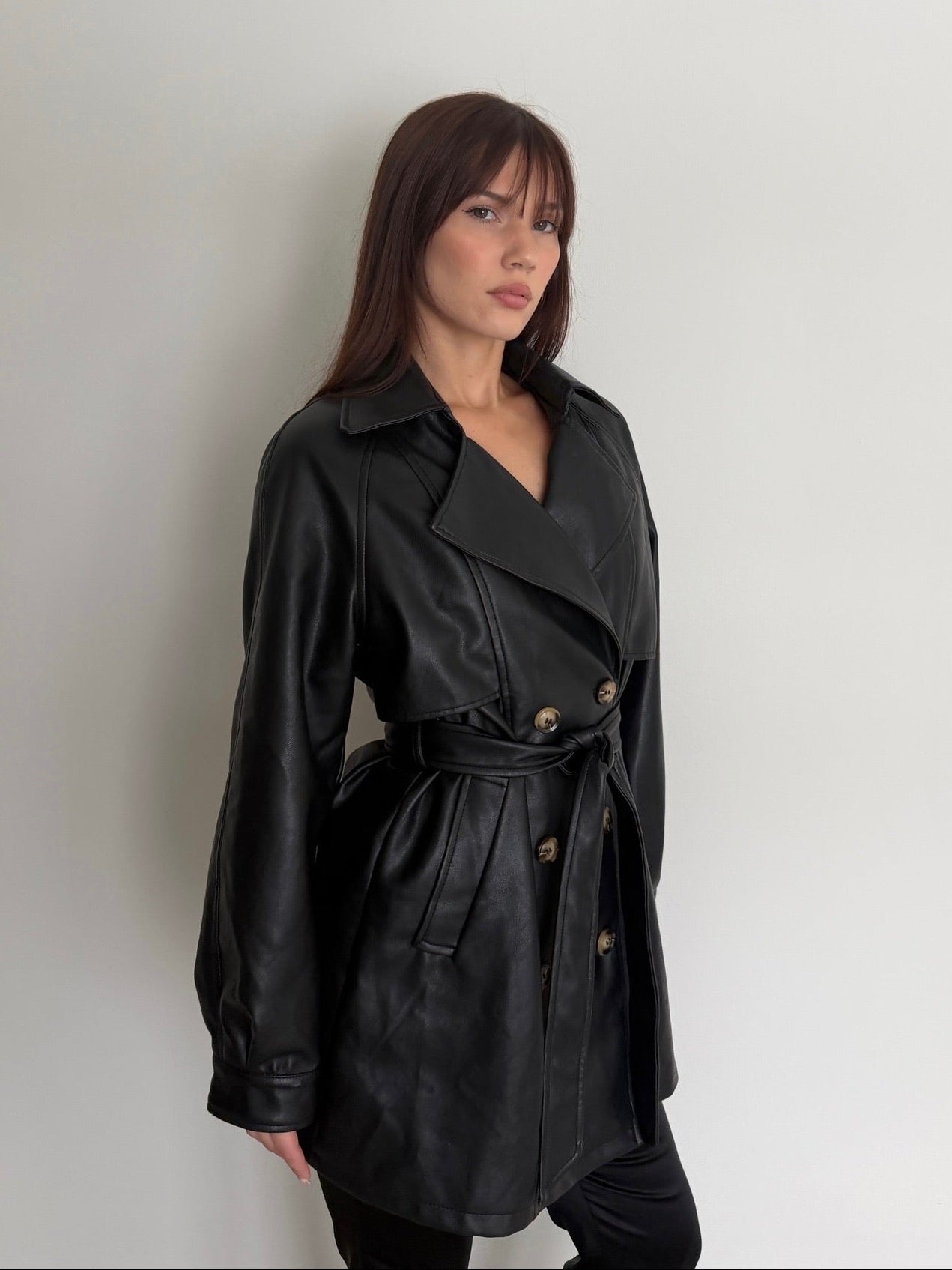 Woman wearing a black leather trench coat against a plain background