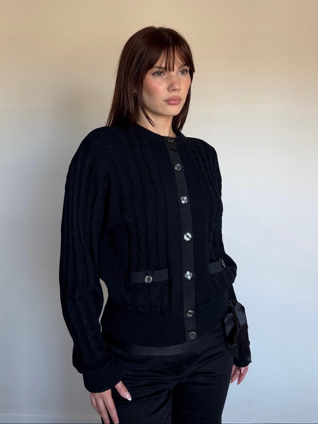 Woman wearing a black cardigan with silver buttons against a plain background