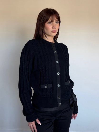 Woman wearing a black cardigan with silver buttons against a plain background
