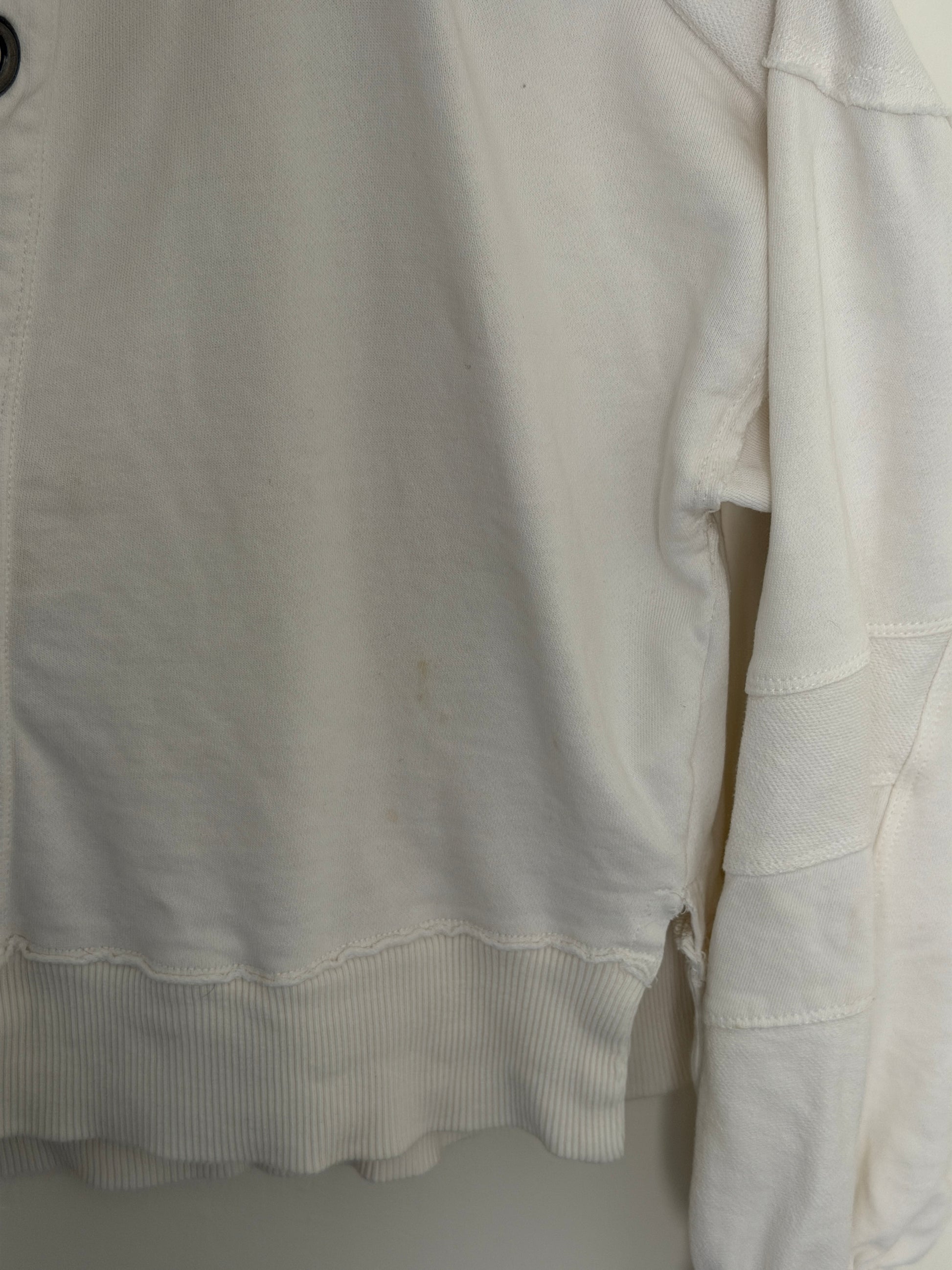 A close-up of a white fabric garment, showing the texture of the material and a ribbed cuff.