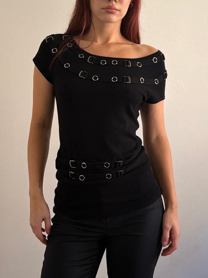 Woman wearing a black outfit with decorative elements against a plain wall.