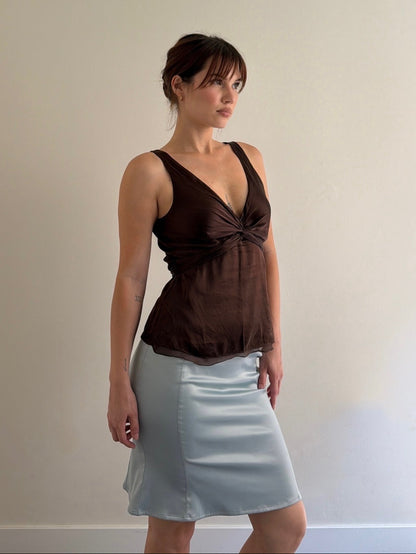 Woman wearing a brown top and light blue skirt against a plain background