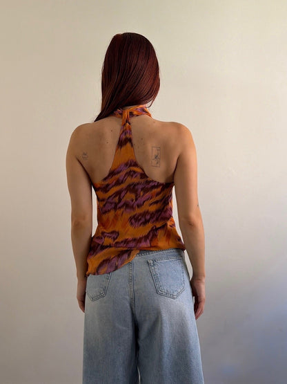 Person wearing a patterned top and denim shorts against a plain wall.