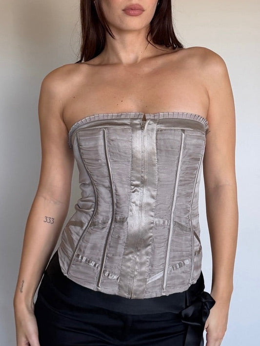 Woman wearing a strapless metallic corset top with black pants against a plain background