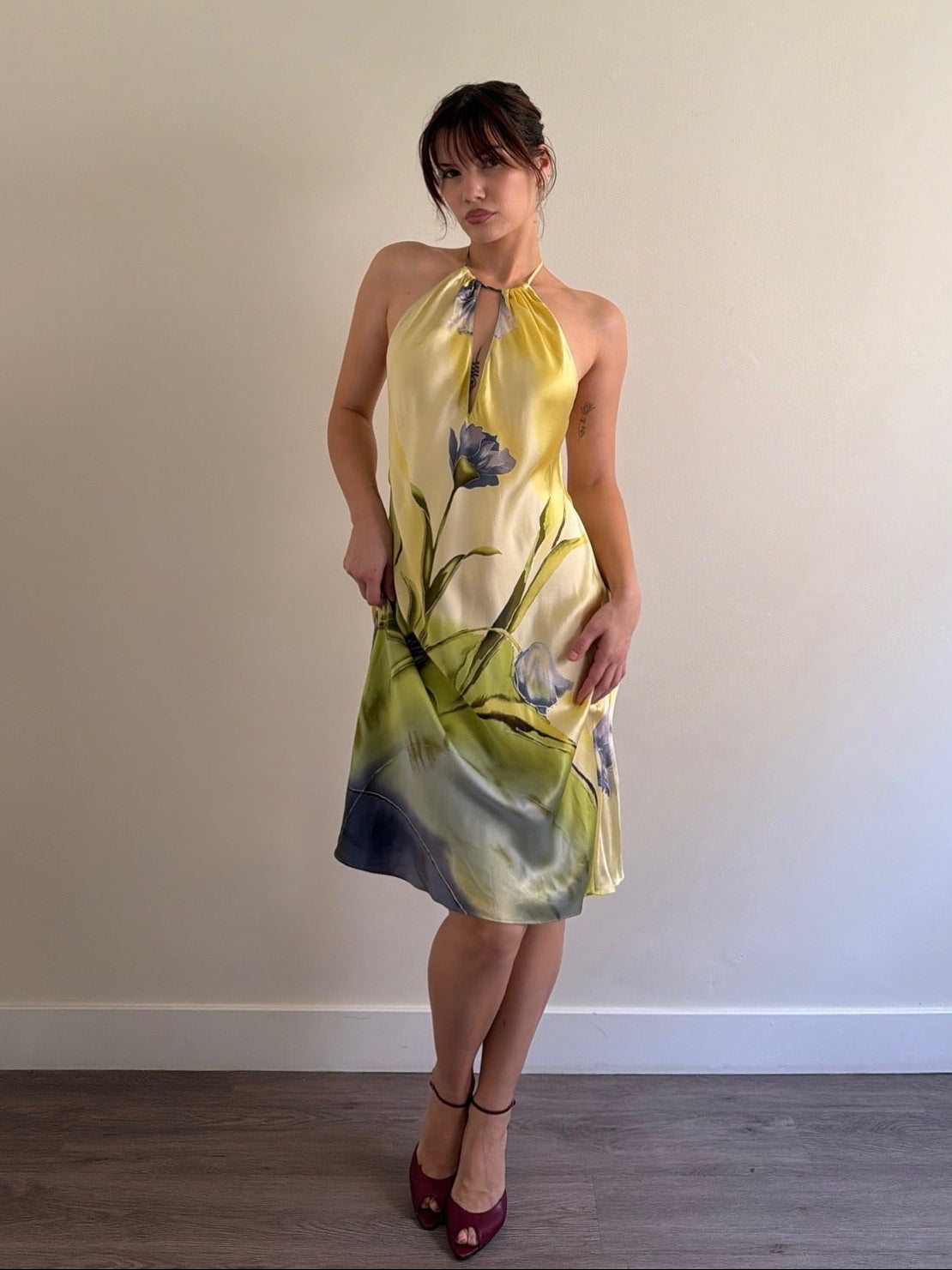 Woman wearing a yellow floral dress against a plain wall.