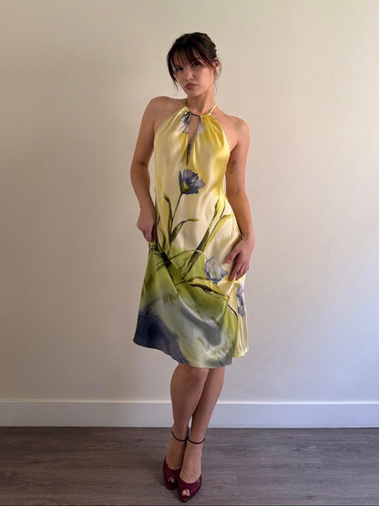 Woman wearing a yellow floral dress against a plain wall.