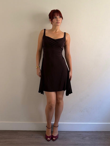 Woman wearing a black dress standing against a plain wall.