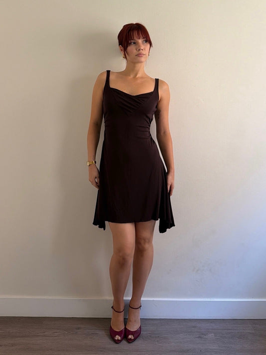 Woman wearing a black dress standing against a plain wall.