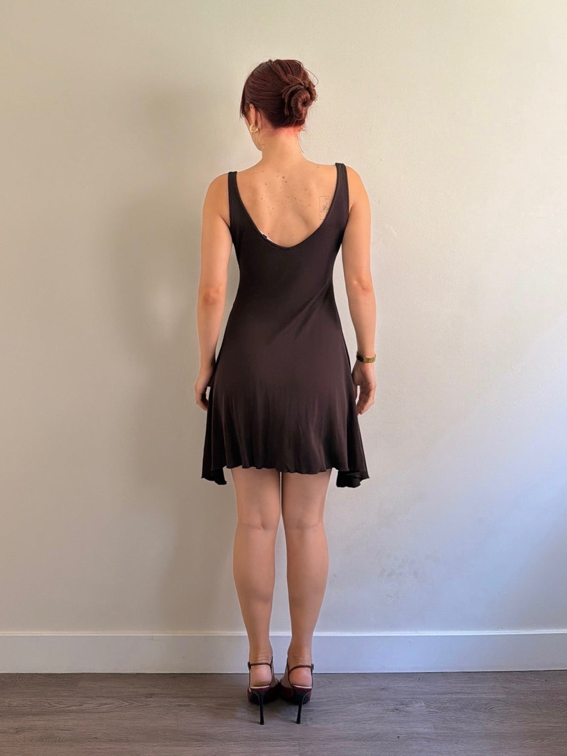 Person wearing a black dress standing against a plain wall.