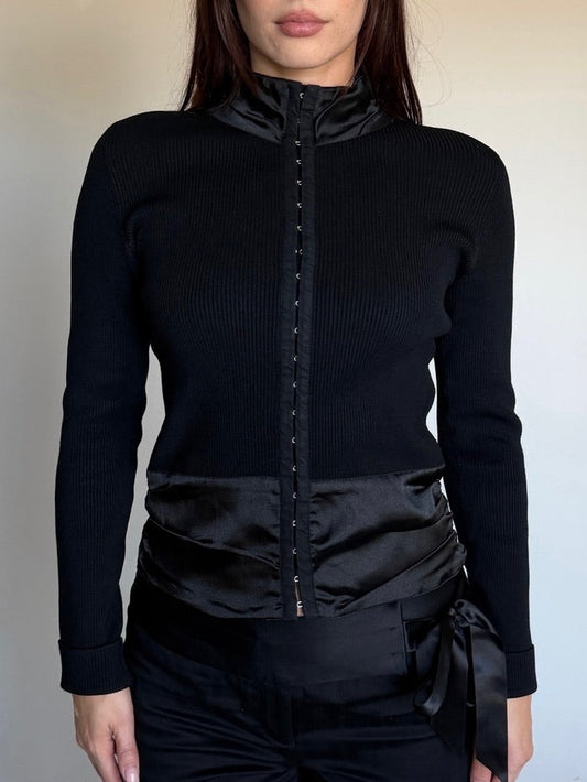 Person wearing a black long-sleeve top with a high collar and black pants against a neutral background