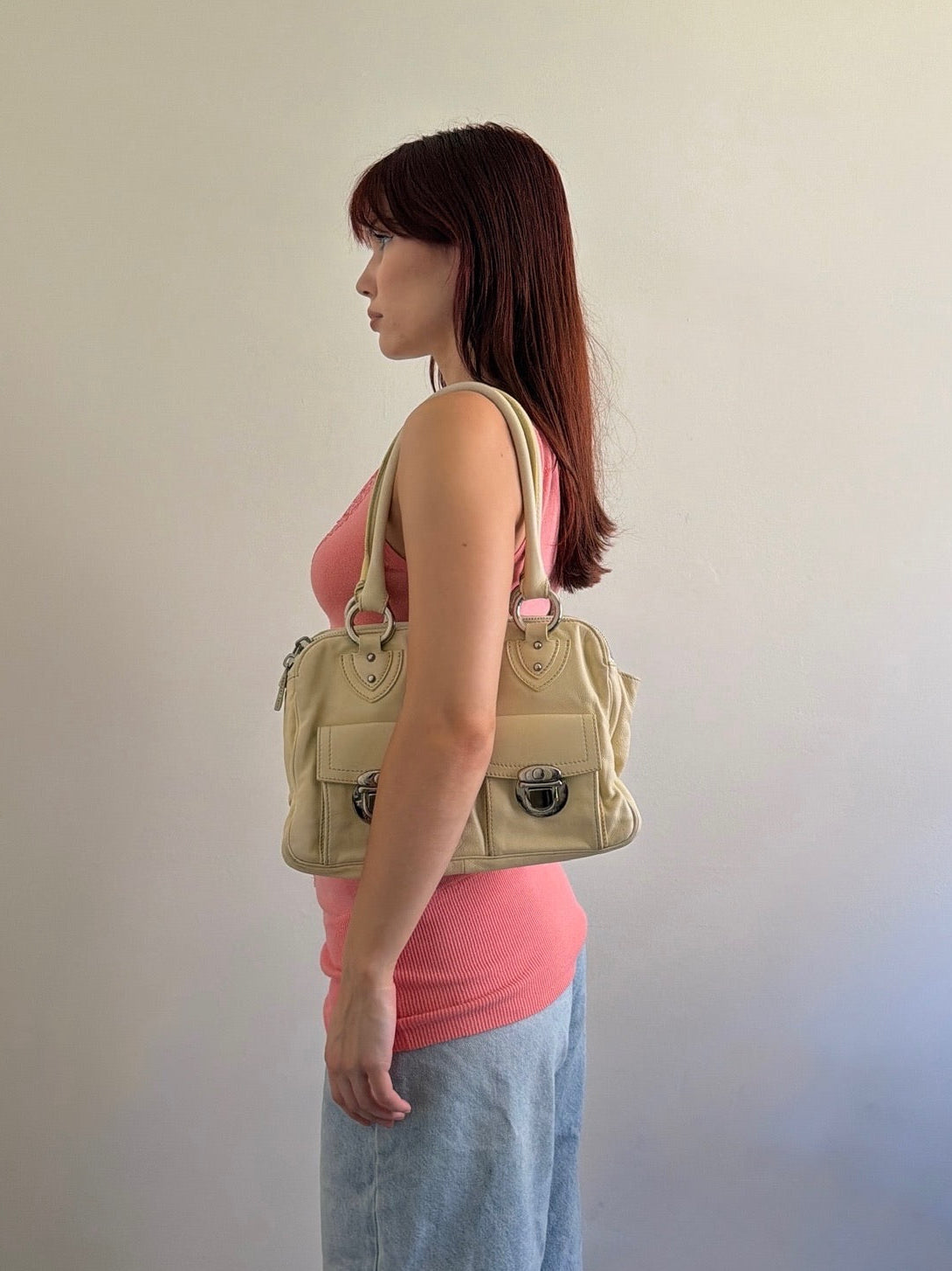 Woman holding a beige handbag against a plain background