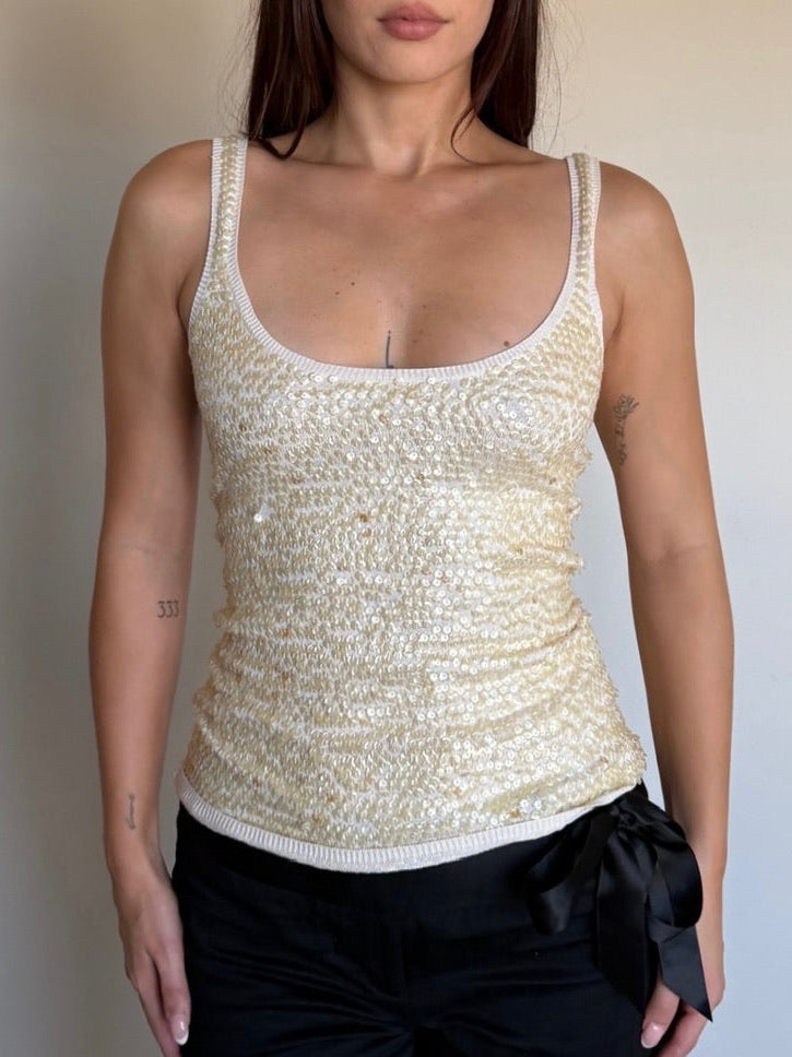 Woman wearing a beige sequin tank top and black pants against a plain background