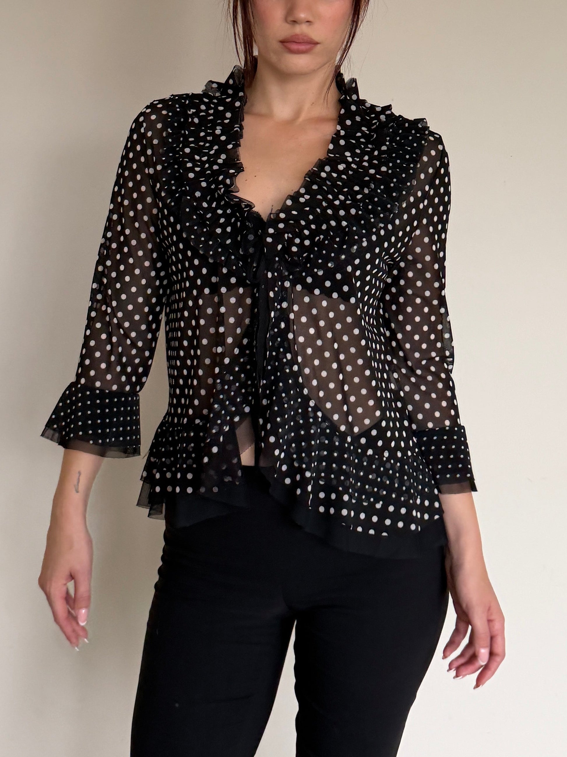 Person wearing a black polka dot top and black pants on a plain background