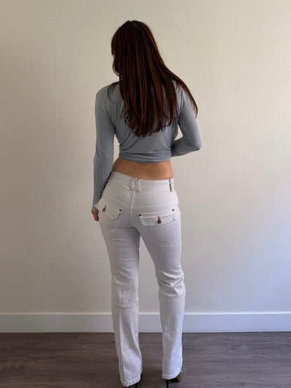 Person wearing a gray long-sleeve top and white pants standing against a plain wall.