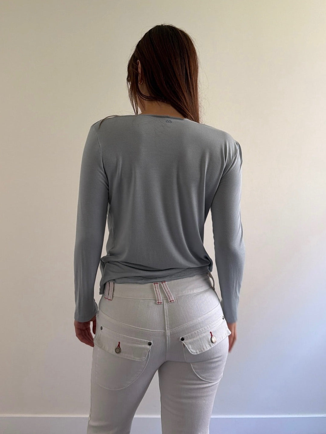 Person wearing a gray long-sleeve top and light gray pants against a plain background