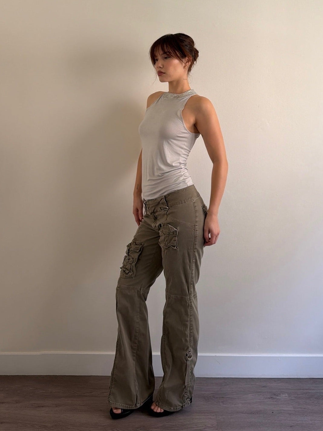 Person wearing a sleeveless top and cargo pants against a plain wall.
