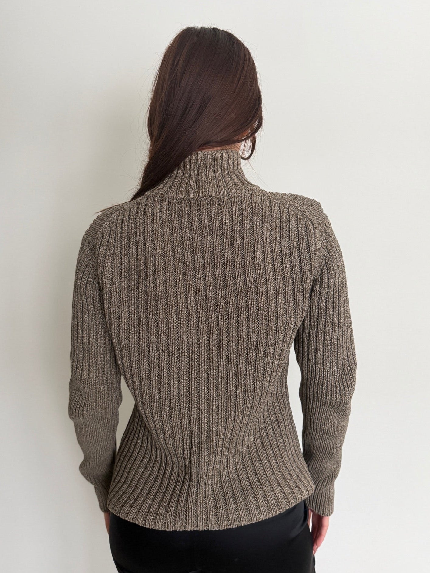 Person wearing a brown ribbed sweater against a white background