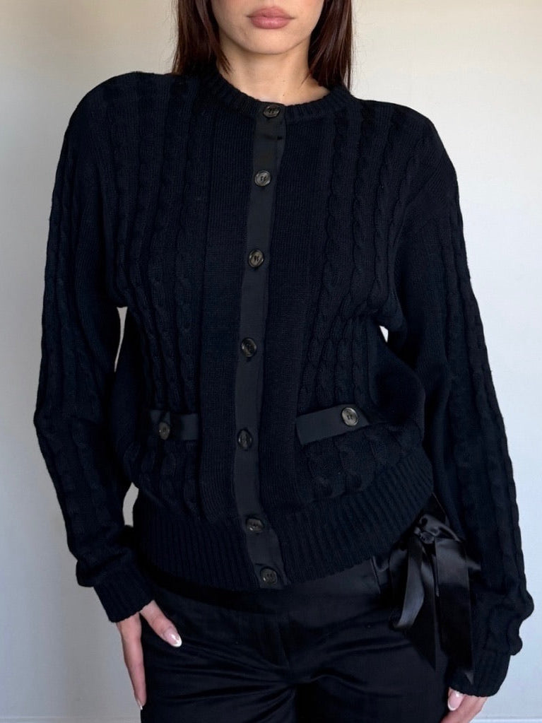 Person wearing a black cable knit wool sweater with a plain background