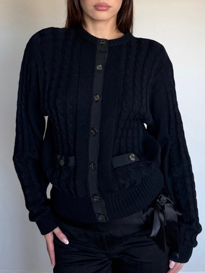 Person wearing a black cable knit wool sweater with a plain background