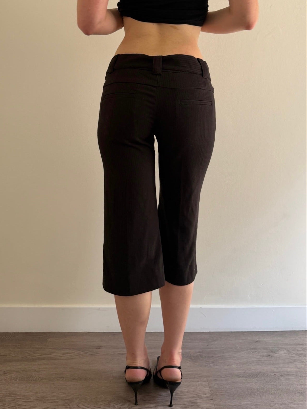 Person wearing black capri pants and a black top against a plain wall.