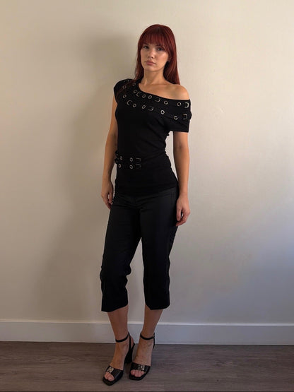 Woman wearing a black outfit with unique design elements against a plain wall.