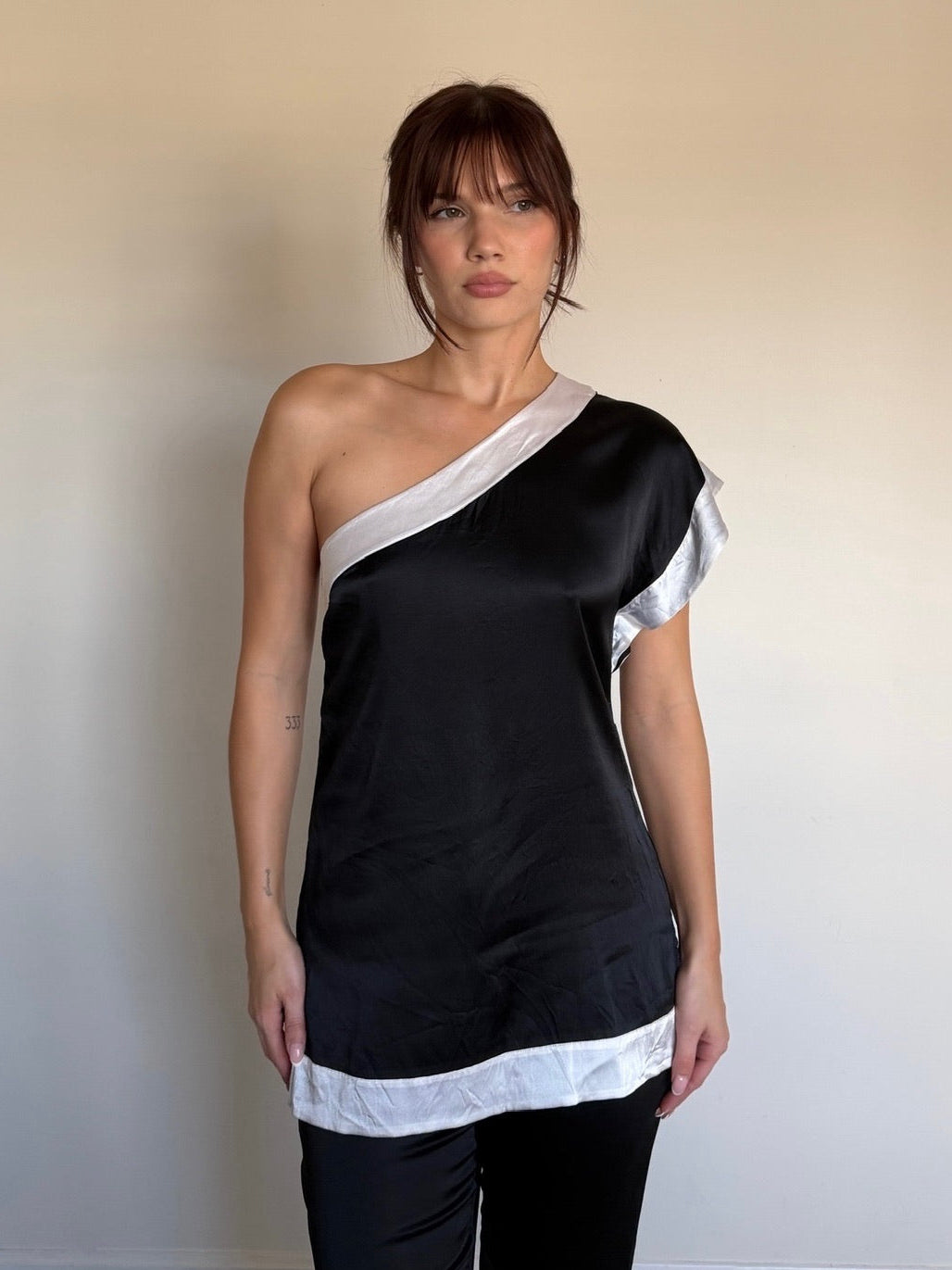 Woman wearing a black and white one-shoulder top against a plain background