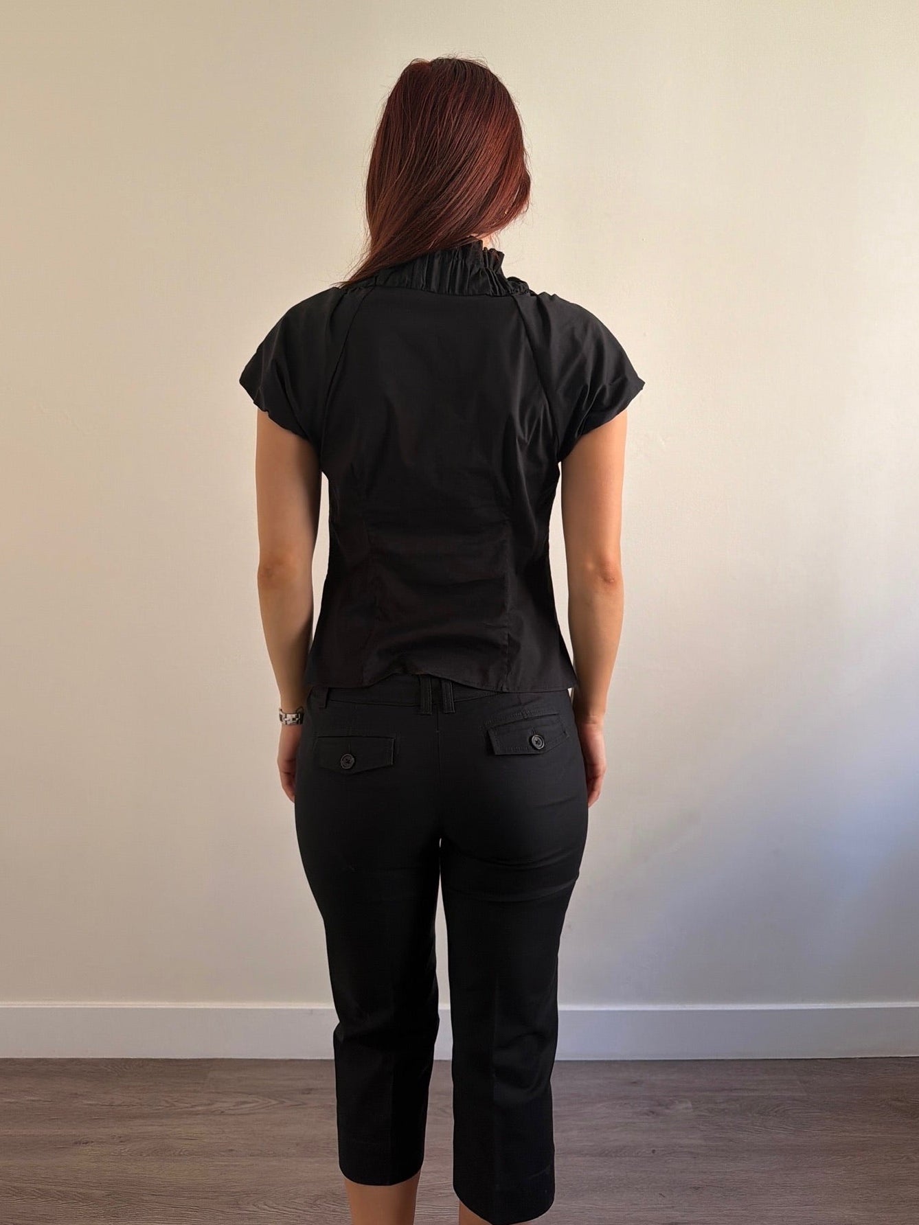Person wearing a black outfit standing against a plain wall.