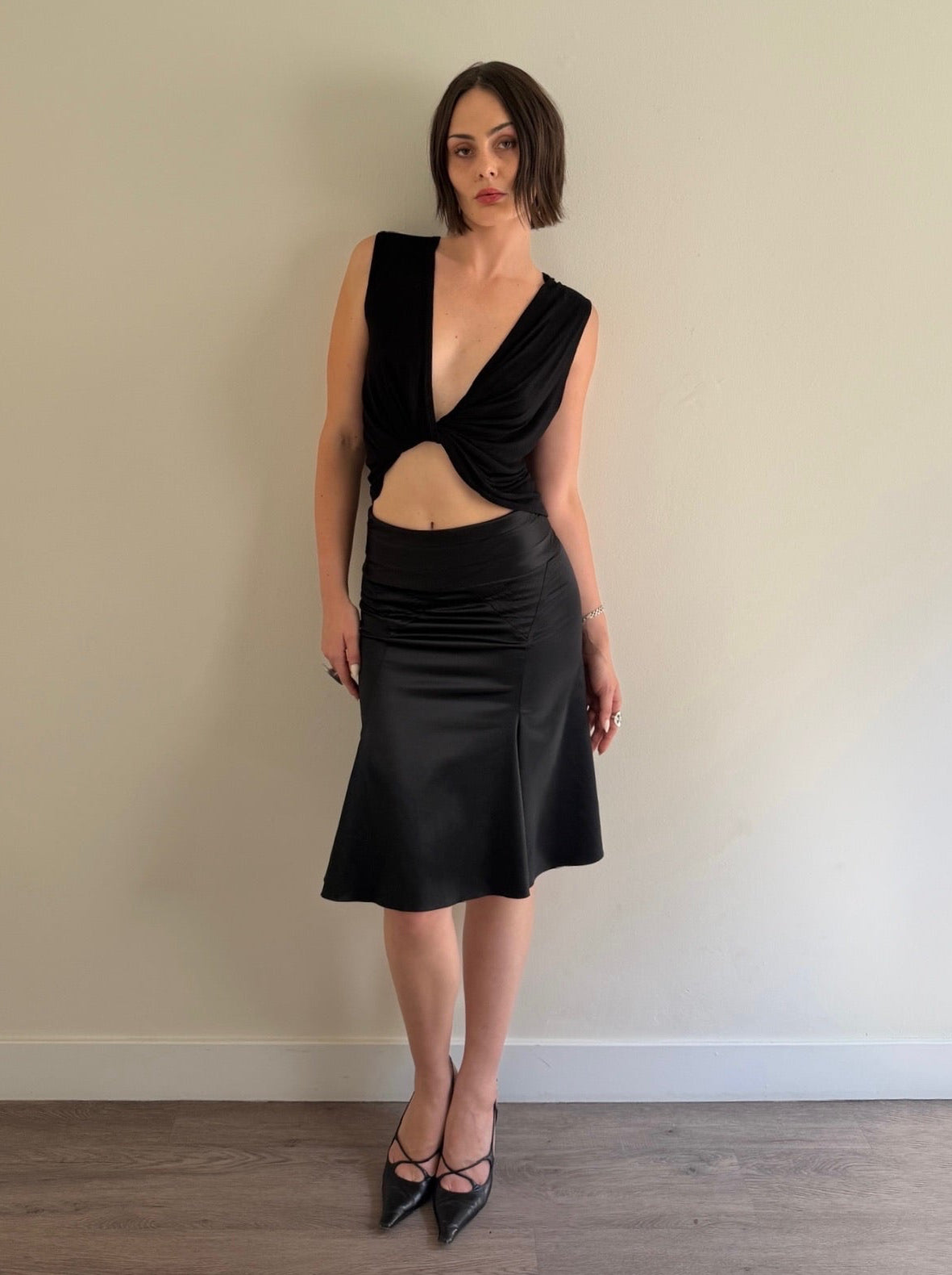 Woman wearing a black dress standing against a plain wall.