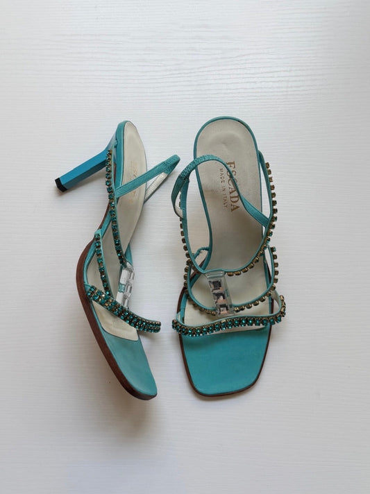 Pair of turquoise high-heeled sandals with rhinestone details on a white background