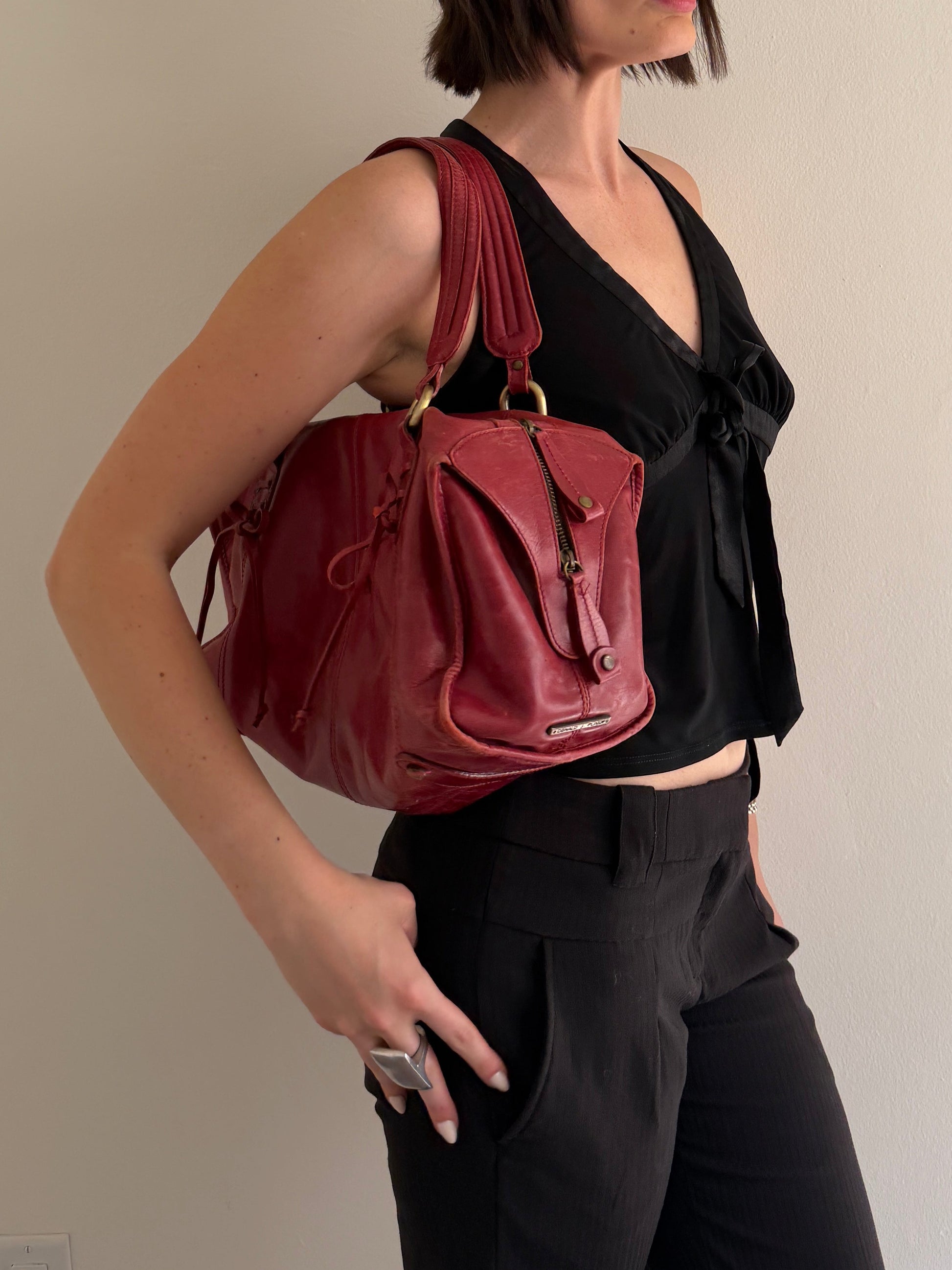 Person wearing a black outfit with a maroon bag on a plain background